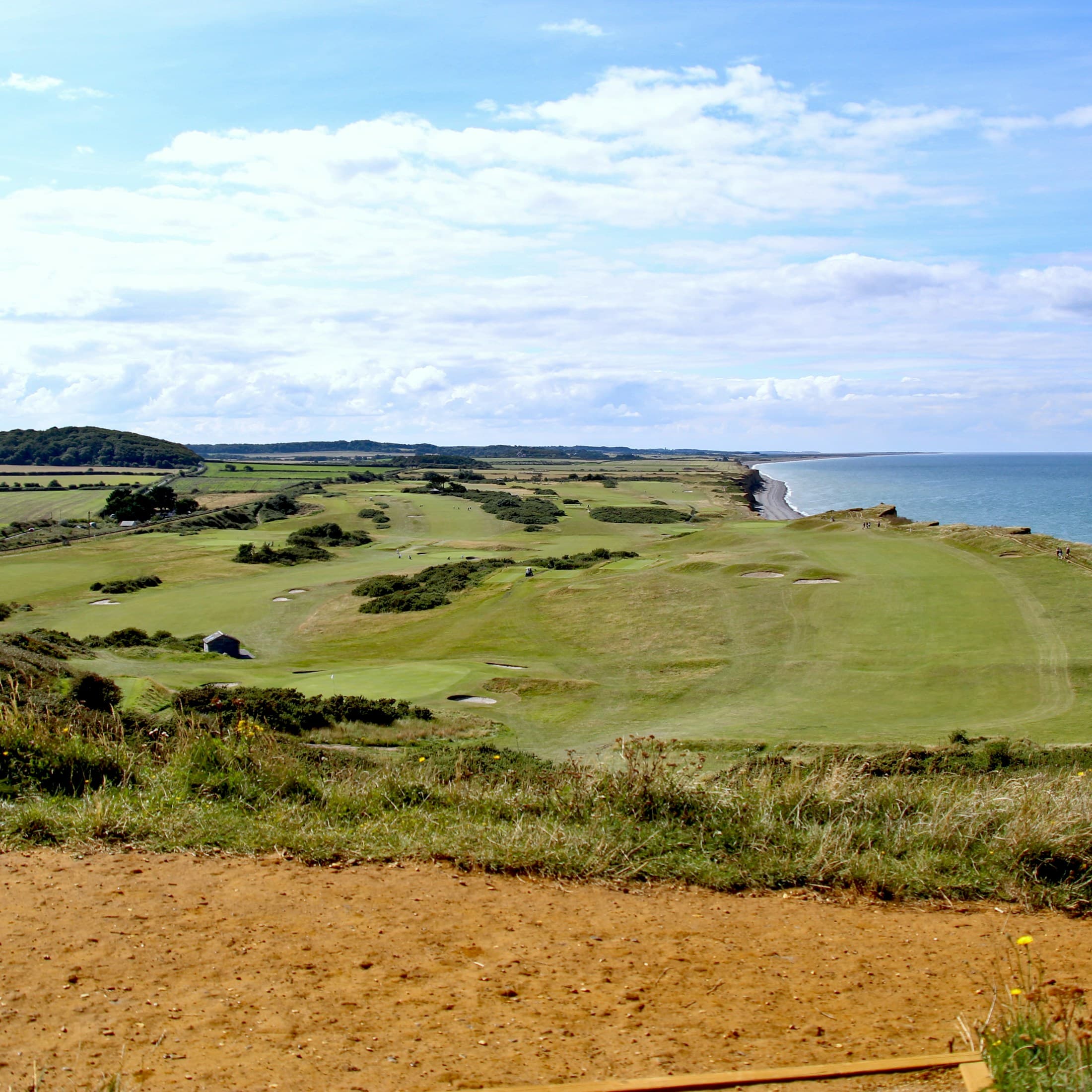 Rolling coastal golf fairways beside the sea under an open summer sky